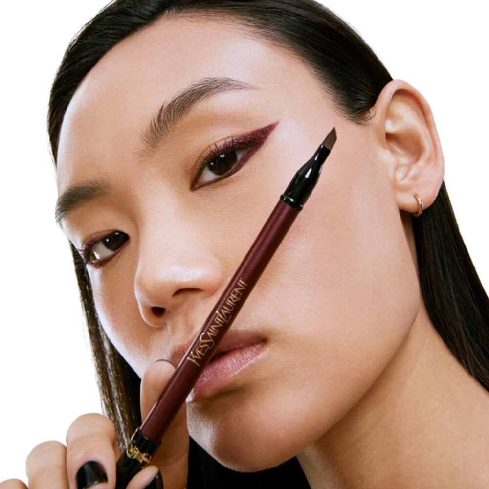 Close-up of a woman holding a YSL eye color product with it applied as eyeliner