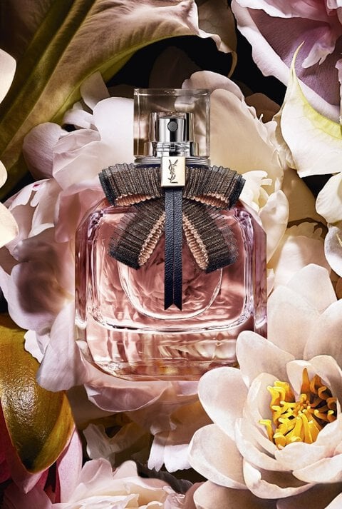 A bottle of YSL perfume with a black bow surrounded by white flowers.
