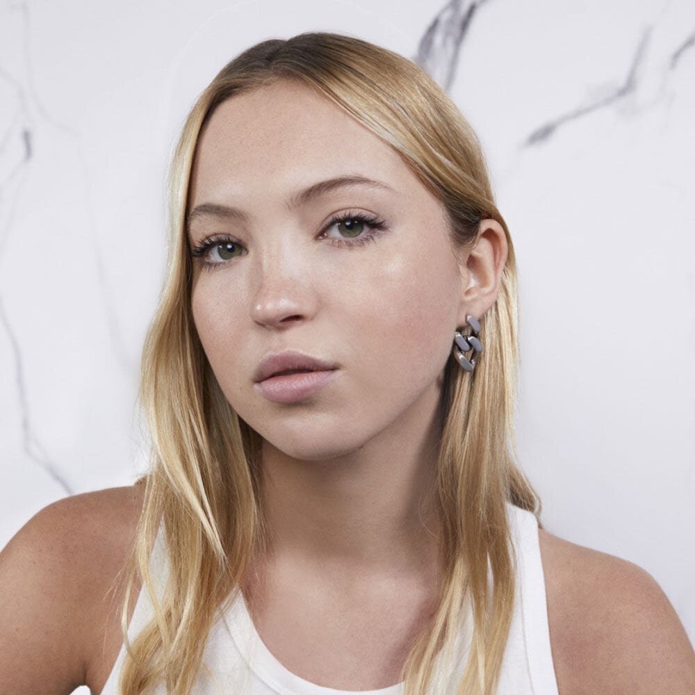 Person with long blonde hair wearing a white tank top and silver earrings.
