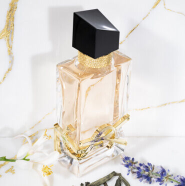 YSL perfume bottle with a black cap and gold accents, surrounded by flowers.