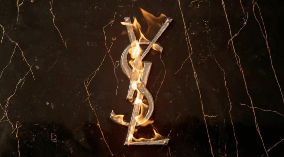 YSL logo on fire against a black marble background.