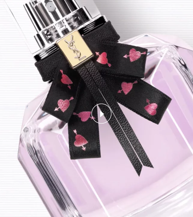 A bottle of YSL perfume with pink liquid and a black bow with heart designs.