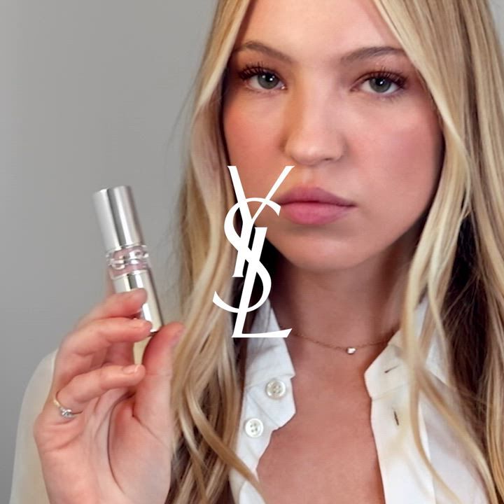 A person holding a silver YSL product with pink details.