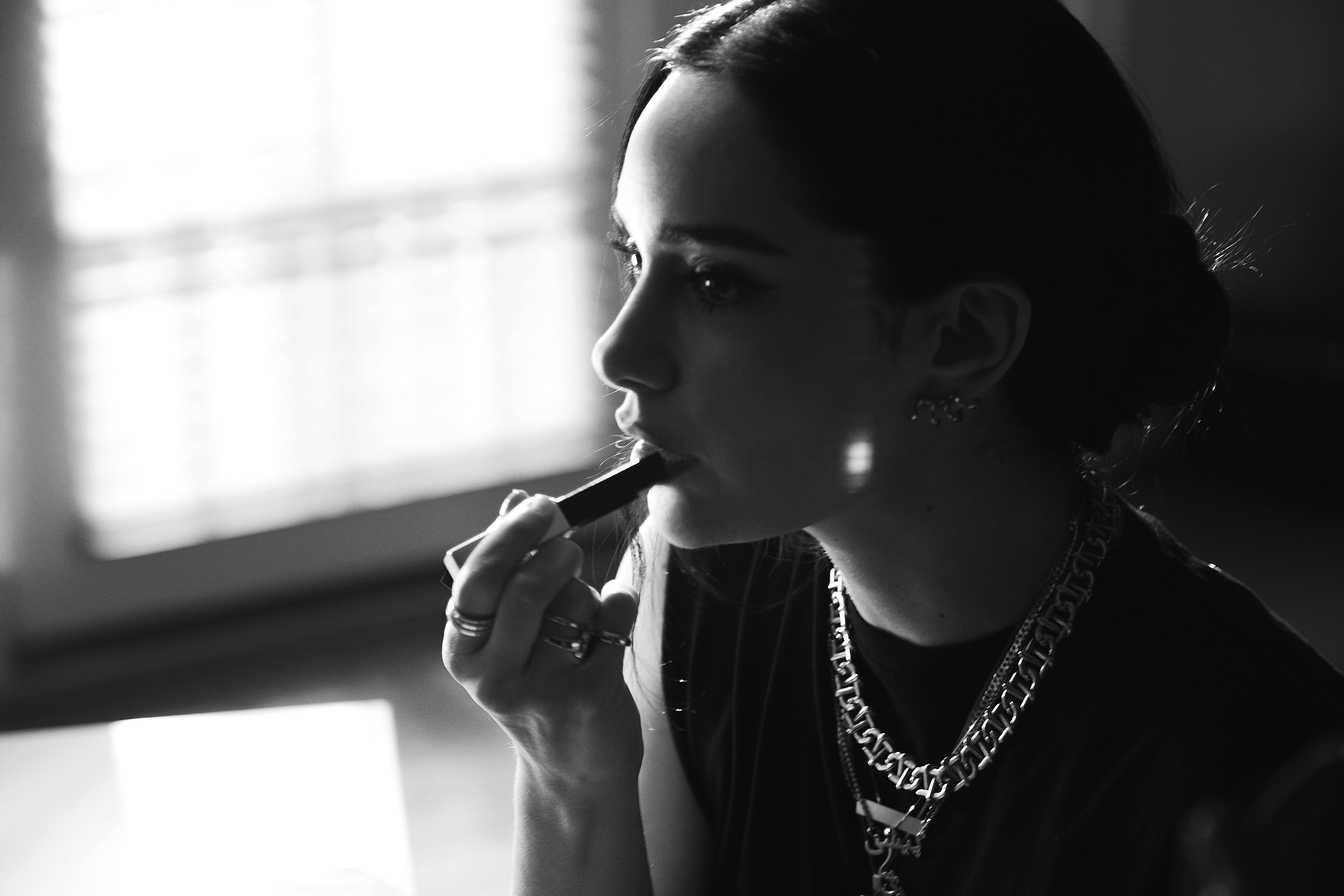 A woman applies lipstick in a black-and-white photo.