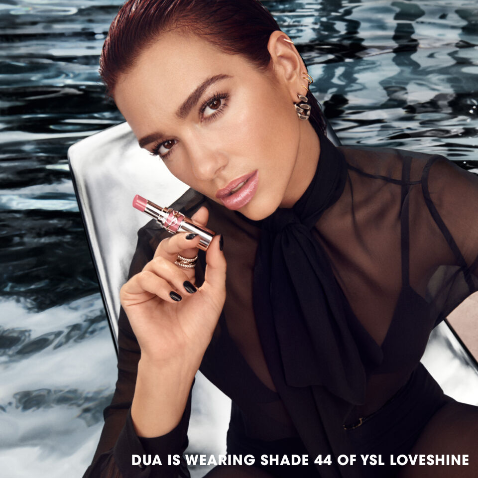 Dua Lipa by a pool holding a lipstick with text 'Dua is wearing shade 44 of YSL Loveshine.'