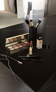 YSL makeup products including an eyeshadow palette, lipstick, and brushes on a black table.