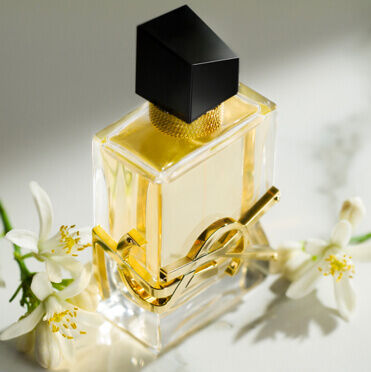YSL perfume bottle with a black cap and gold accents, surrounded by white flowers.