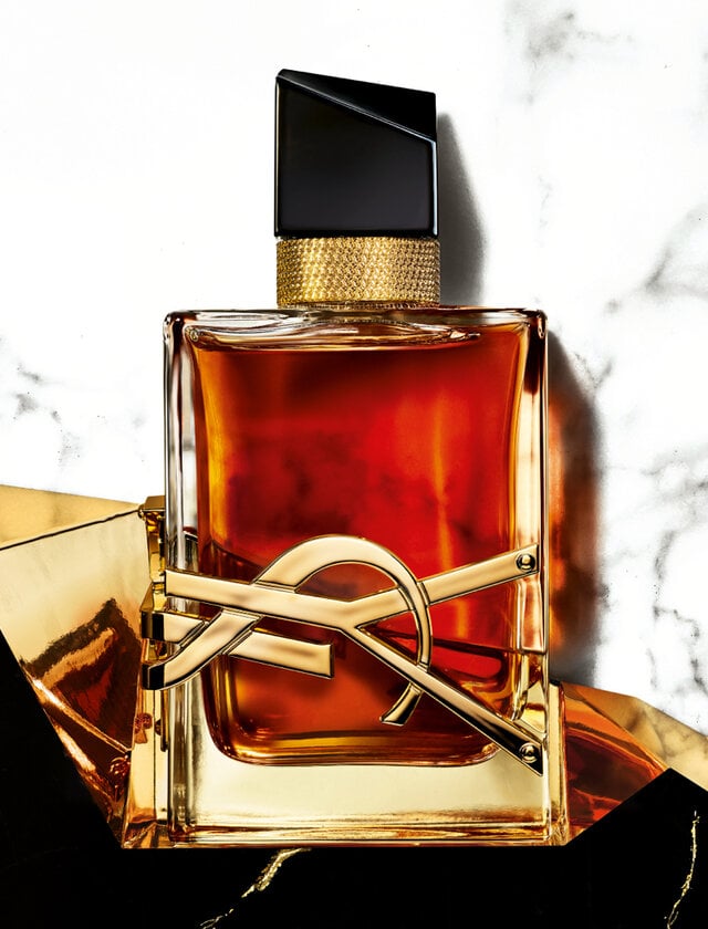 Rectangular YSL perfume bottle with amber liquid. A gold logo sits on the front against a marble background.