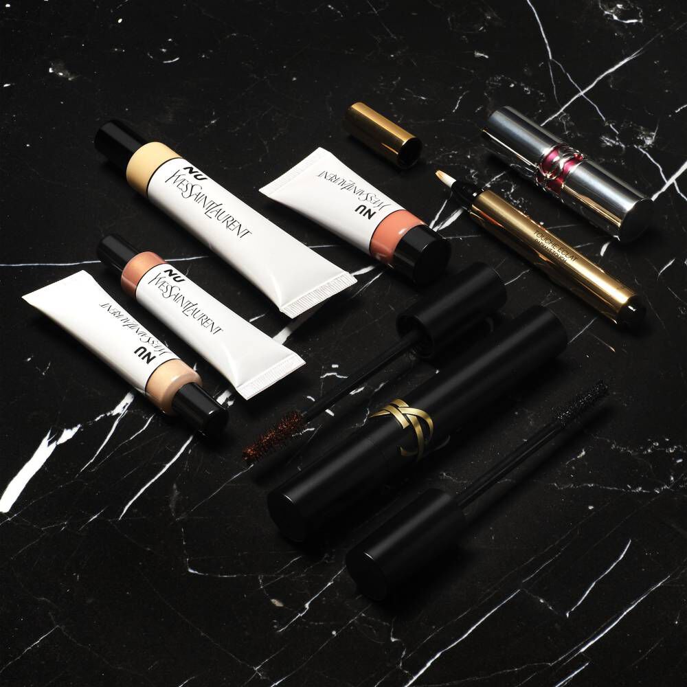 YSL Nu foundation and concealer tubes, mascara, and other makeup products on a black marble surface.