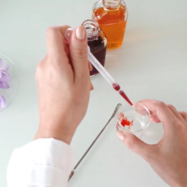 Person using a dropper with red liquid and bottles in the background.