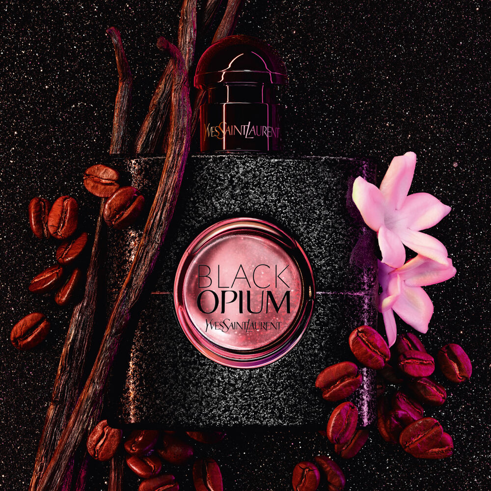 YSL Black Opium perfume bottle surrounded by coffee beans, vanilla pods, and a white flower.