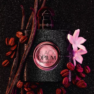 Yves Saint Laurent Black Opium perfume bottle with coffee beans, vanilla pods, and a white flower on a dark background.