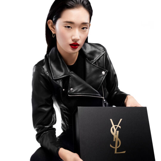 A person in a black leather jacket holds a black YSL box.