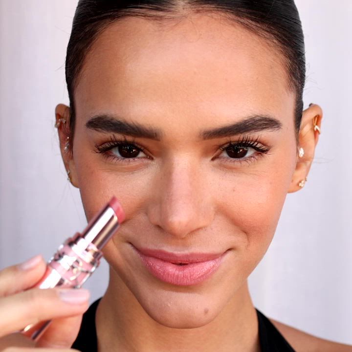 A person holding a silver YSL product with pink details.