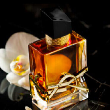 YSL perfume bottle with a black cap and gold accents, surrounded by white orchids.