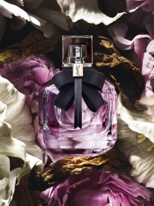 A bottle of YSL perfume with a black bow, surrounded by flowers