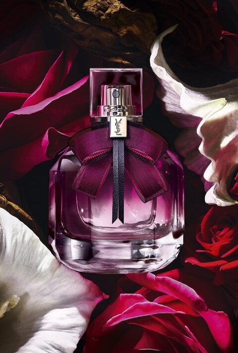 A bottle of YSL perfume with a purple bow surrounded by red and white flowers.