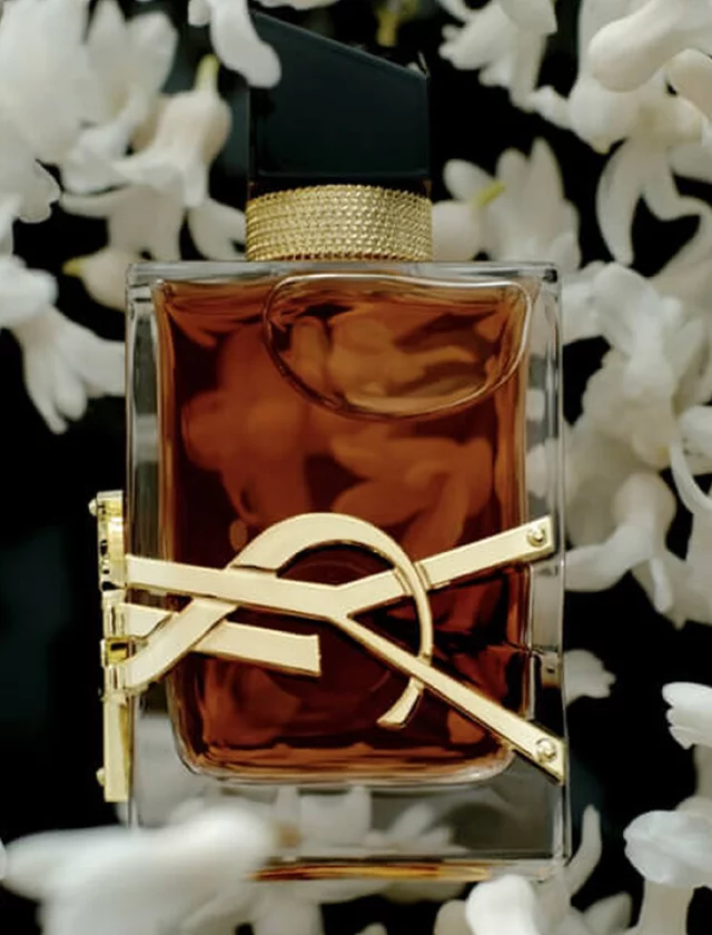 YSL perfume bottle with amber liquid surrounded by white flowers.