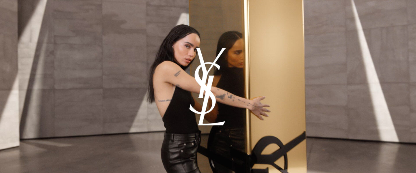 Zoe Kravitz standing next to a large gold YSL logo.