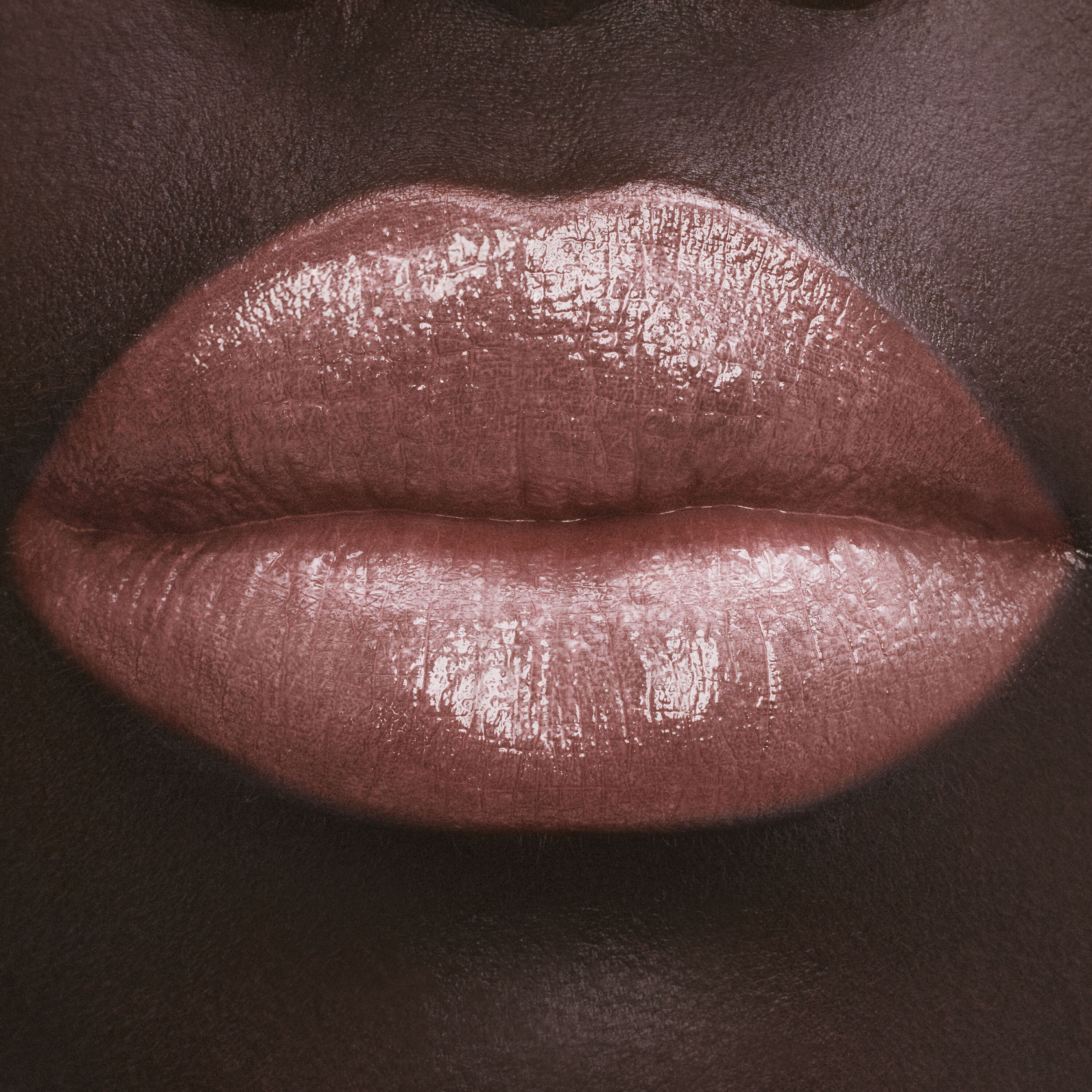 Close-up of lips with glossy nude lipstick on dark skin.