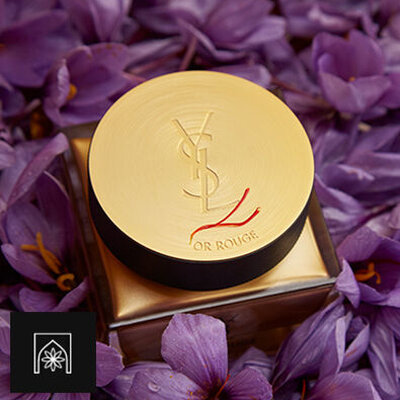 A jar of YSL Or Rouge cream surrounded by purple flowers.