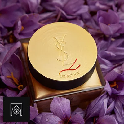 A jar of YSL Or Rouge cream surrounded by purple flowers.