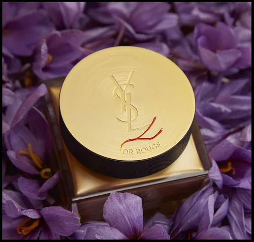 YSL Or Rouge cream jar with a gold lid surrounded by purple flowers.