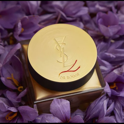 YSL Or Rouge cream jar with a gold lid surrounded by purple flowers.