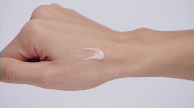 A hand with a swatch of white cream on the back.