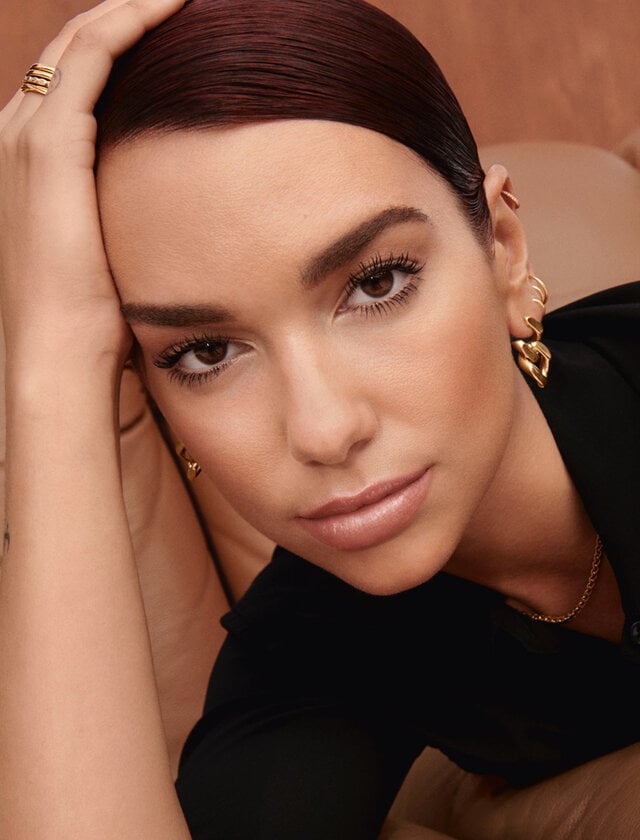 A person lying on a couch with text '24HR Wear Sunkissed Glow. Subtle Shimmer. Ultra Buildable & Blendable.'