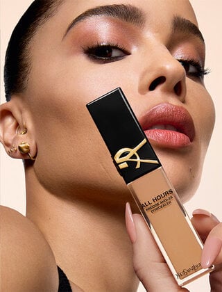 Person holding a tube of YSL All Hours concealer against a peach background.
