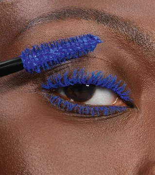 Close-up of an eye with blue mascara being applied to the lashes.