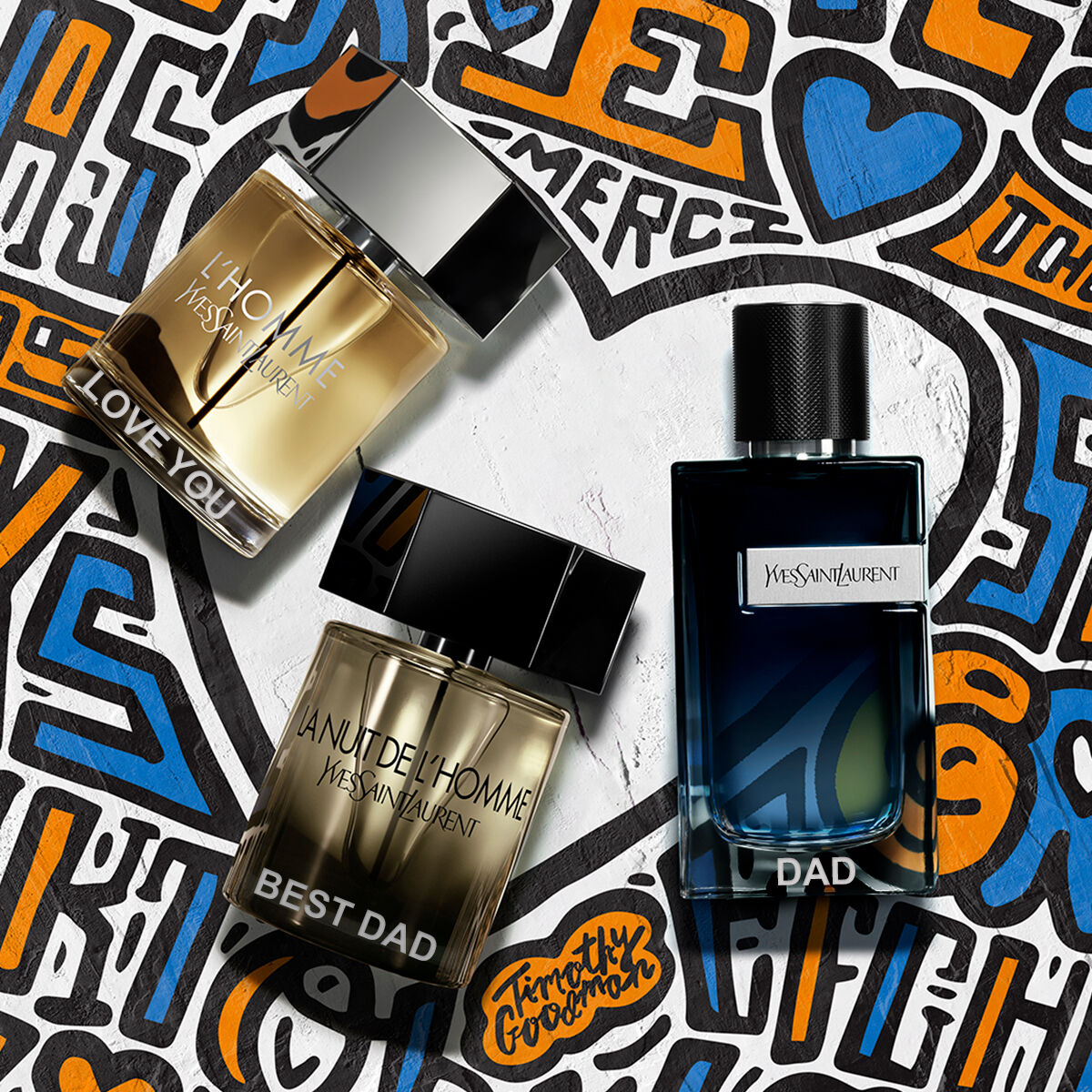 Three YSL L'Homme perfume bottles labeled 'LOVE YOU,' 'BEST DAD,' and 'DAD' against a colorful graffiti background.