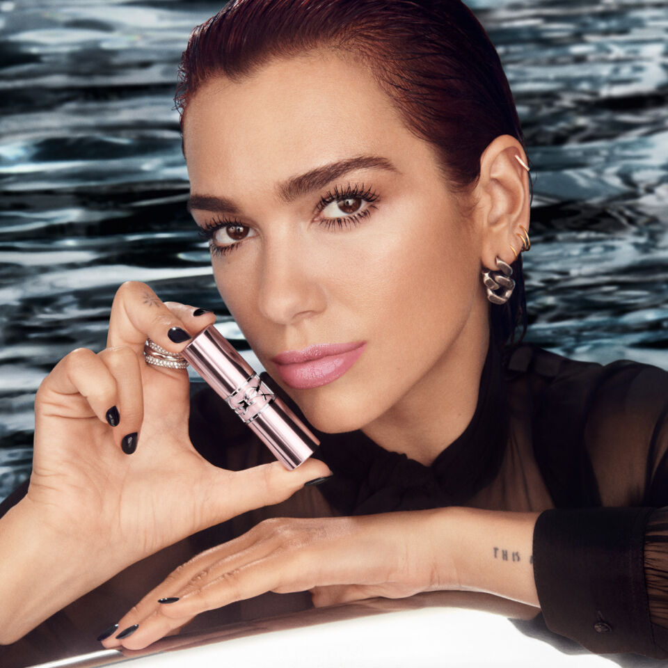Dua Lipa holding a lipstick by a pool.