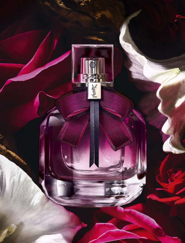 YSL perfume bottle with a purple bow surrounded by red and white flowers.