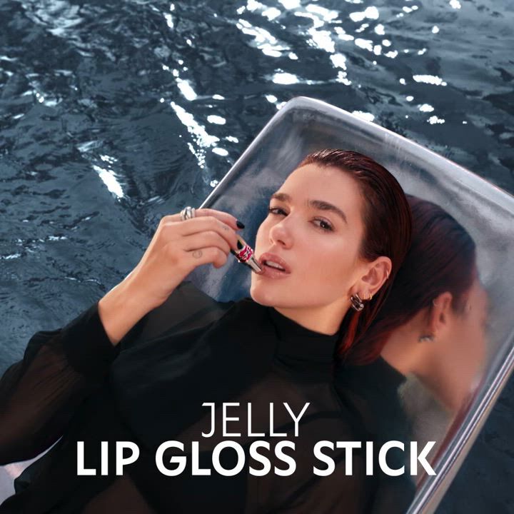 Person lounging by a pool holding a lip gloss stick with the text 'JELLY LIP GLOSS STICK.'