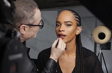 A makeup artist applies makeup to a person in a studio setting.