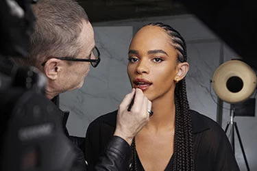 A makeup artist applies makeup to a person in a studio setting.