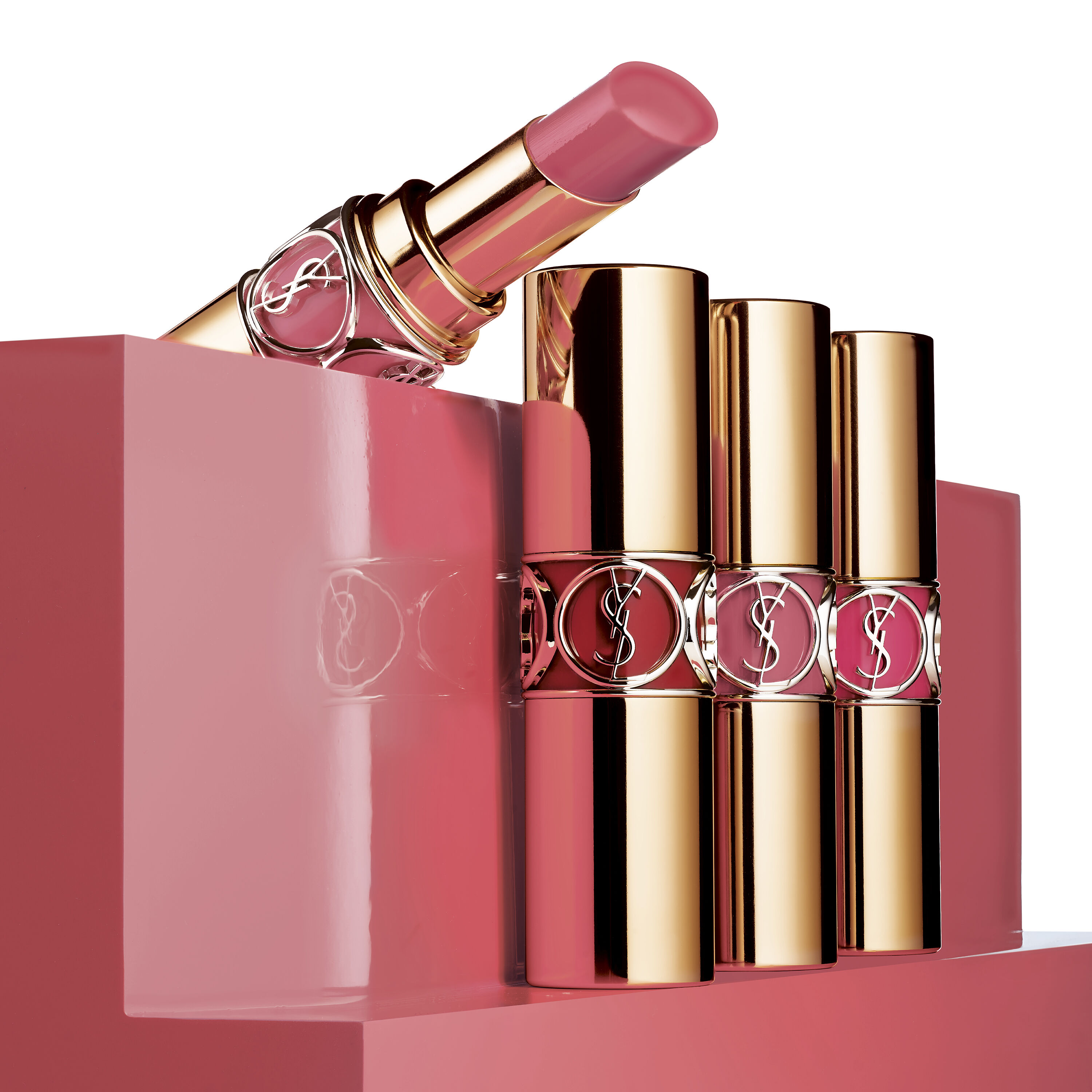 Four tubes of YSL lipstick in pink shades displayed on a pink stand.