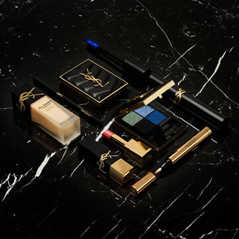 A collection of YSL makeup products on a black marble surface.