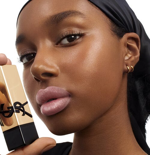 A woman holding a gold YSL lipstick near her face.