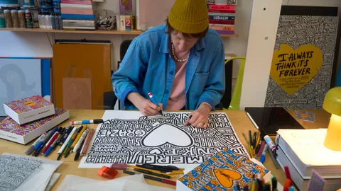 A person drawing on a large piece of paper surrounded by art supplies.
