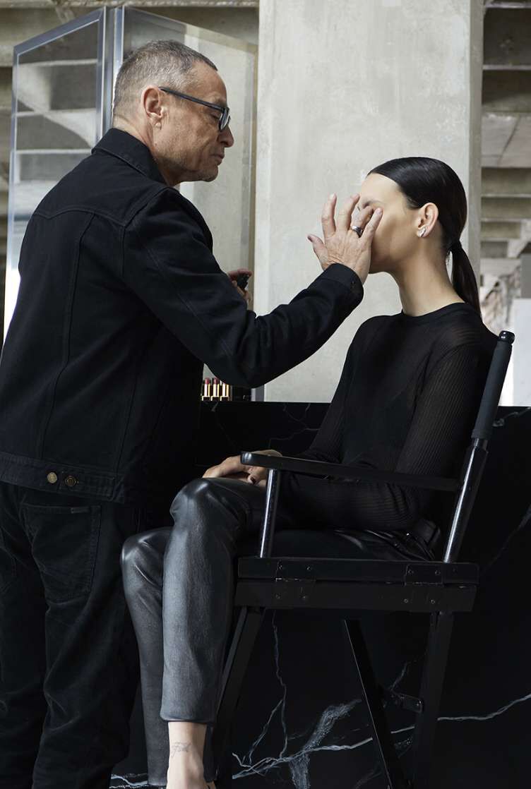 A makeup artist applying makeup to a seated model.