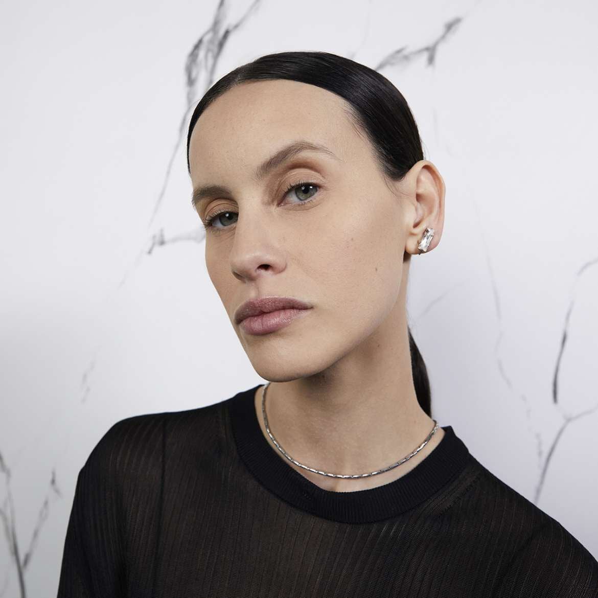 Person wearing earrings and a necklace against a marble background.