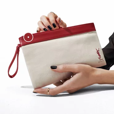 Hands holding a white and red YSL Beauté pouch.