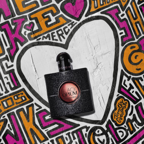A bottle of YSL Black Opium perfume against a colorful graffiti background with a white heart.