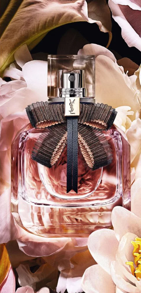 Rectangular YSL perfume bottle with pink liquid and a black bow, surrounded by flowers.