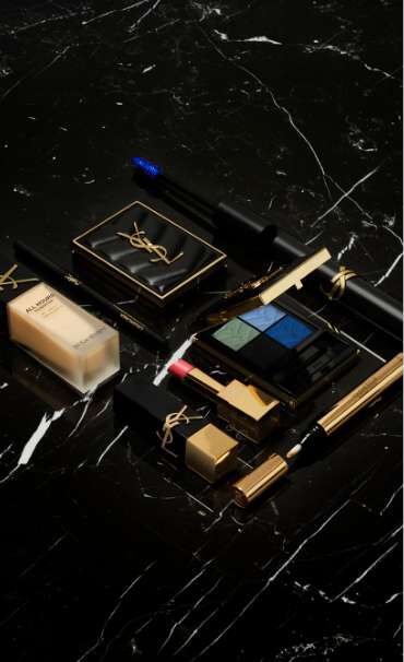 YSL makeup products including foundation, eyeshadow, and lipstick on a black marble surface.