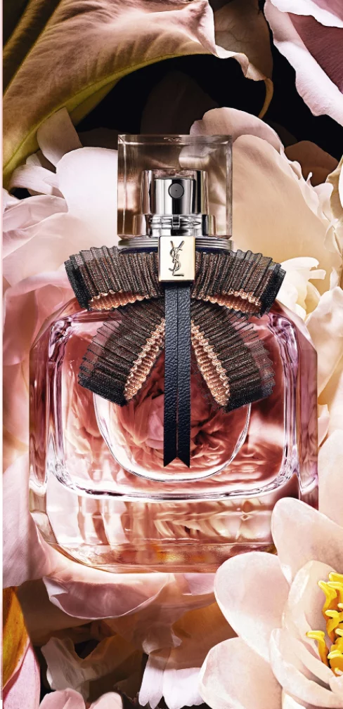 A pink YSL perfume bottle with a black bow surrounded by flowers.