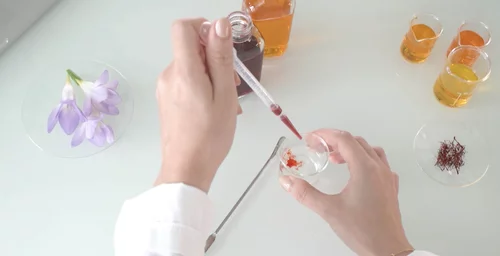 Hands using a dropper to mix liquids in a lab setting with flowers and beakers.